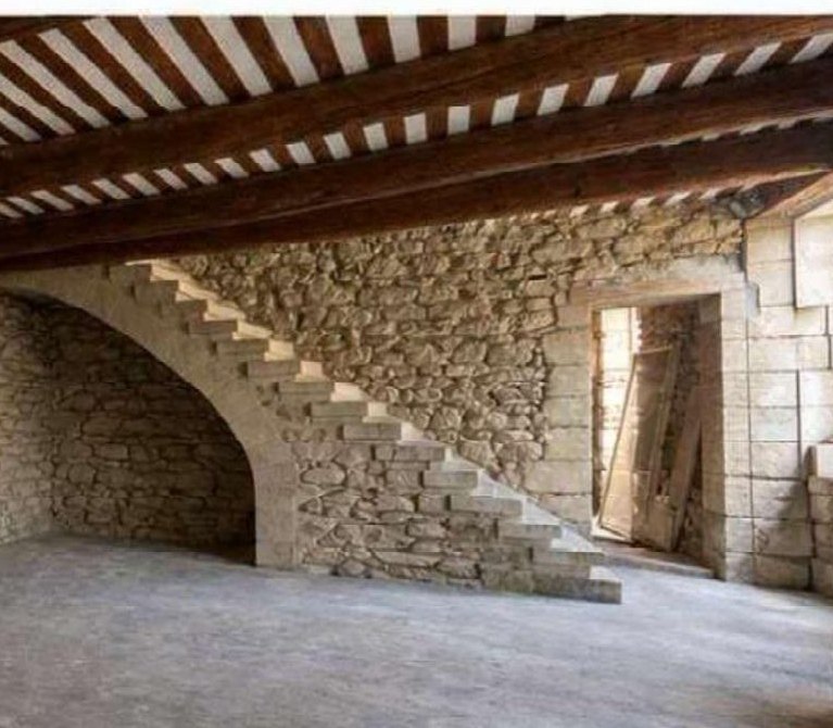 Espace intérieur voûté avec escalier de pierre et plafond à poutres